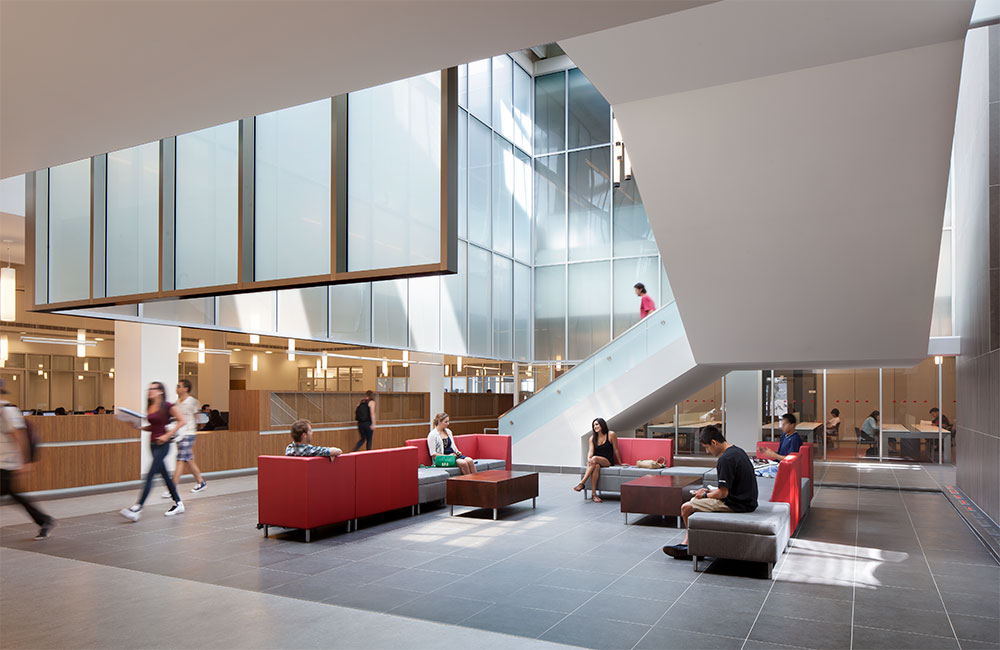 Image 1. Stairs wrap around a 2-story atrium with red and grey couches located on the ground floor area. Frosted glass panels supported by metal frames cover the second-floor gallery, offering protection from direct sunlight and sounds from the first floor.