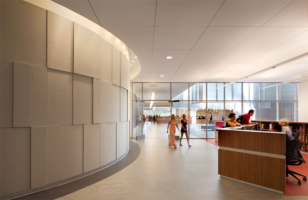 Image 5. Library entrance with service desk on the right side and a curved wall with subtle rectangular relief patterns on the left side.