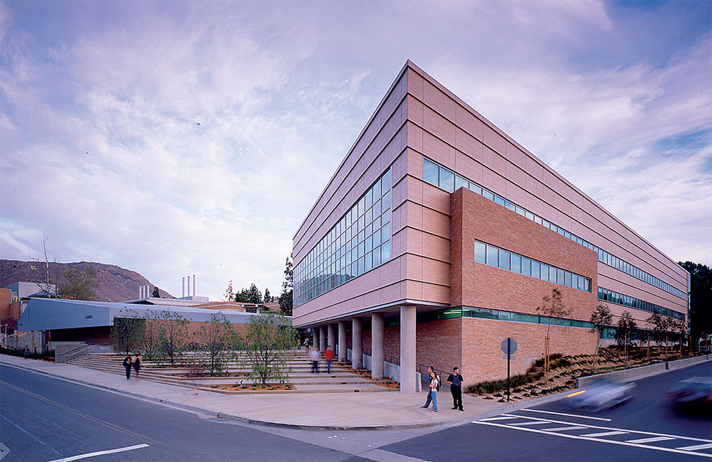 Image 3. A 3-story modern sandstone-colored building is located on the right.  A 1-story modern sandstone-colored building with angular light grey metal roof is located on the left. A gently sloped plaza sits between the 2 structures.