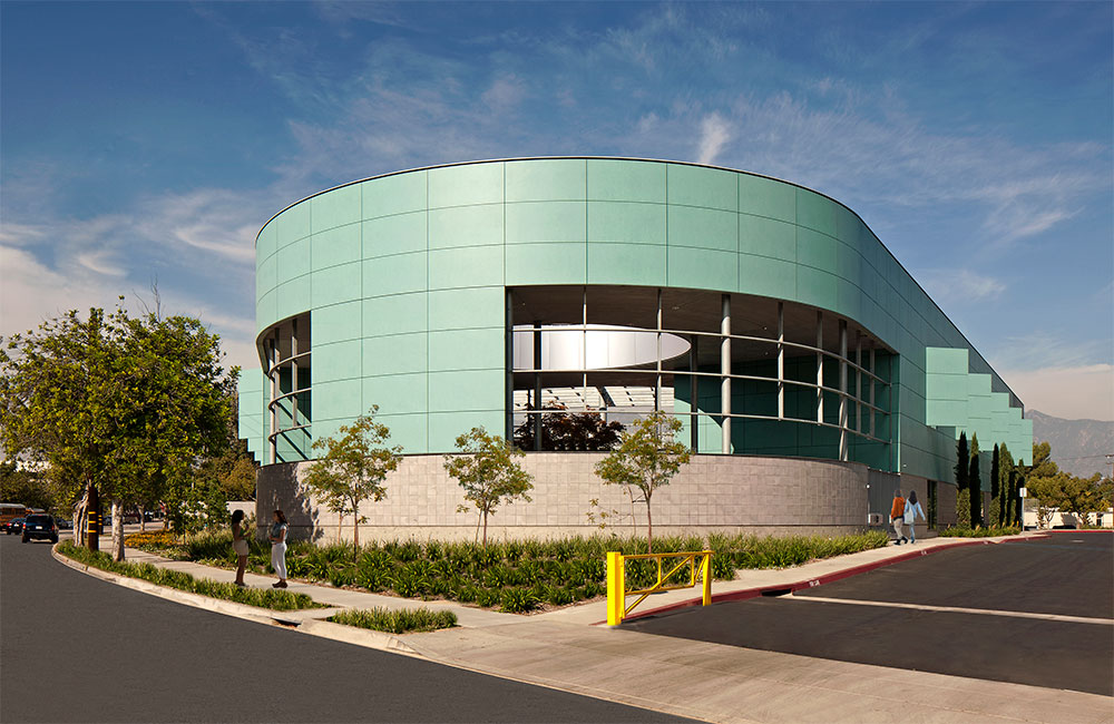 Image 1. A 2-story modern building with turquoise-colored tiles on the upper level and concrete-colored tiles on the first floor. The end of the building is rounded with large openings allowing views of the cylindrical courtyard inside.