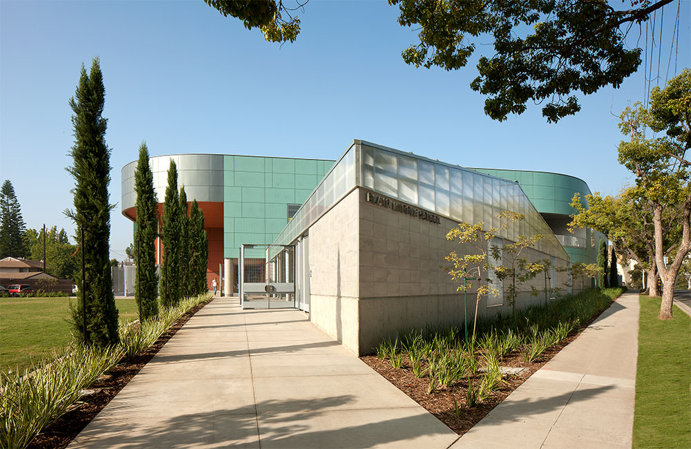 Image 7. Corner view of building showing a mixture of turquoise-colored panels, concrete-colored tiles, metallic panels and reddish-brown accent walls.