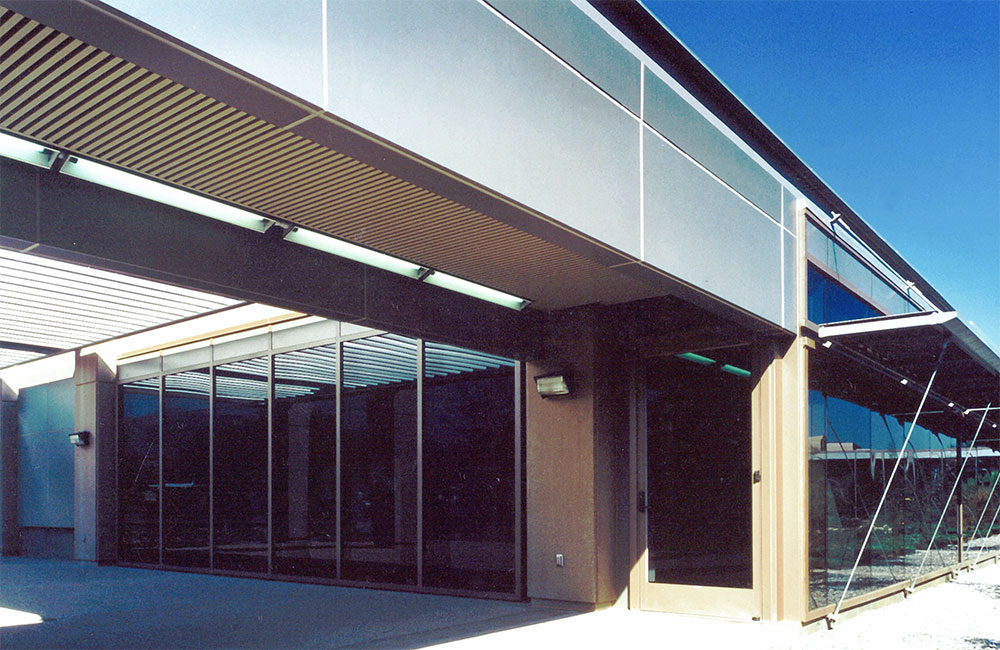 Image 5. Corner view of 1-story glass and steeel modern building with horizontal canopy running along right side.
