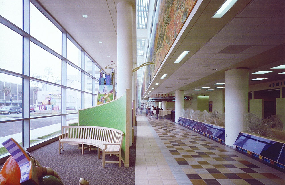 Image 4. Waiting area and walkway with glass curtain wall on the left and multi-colored floor tiles on the right.